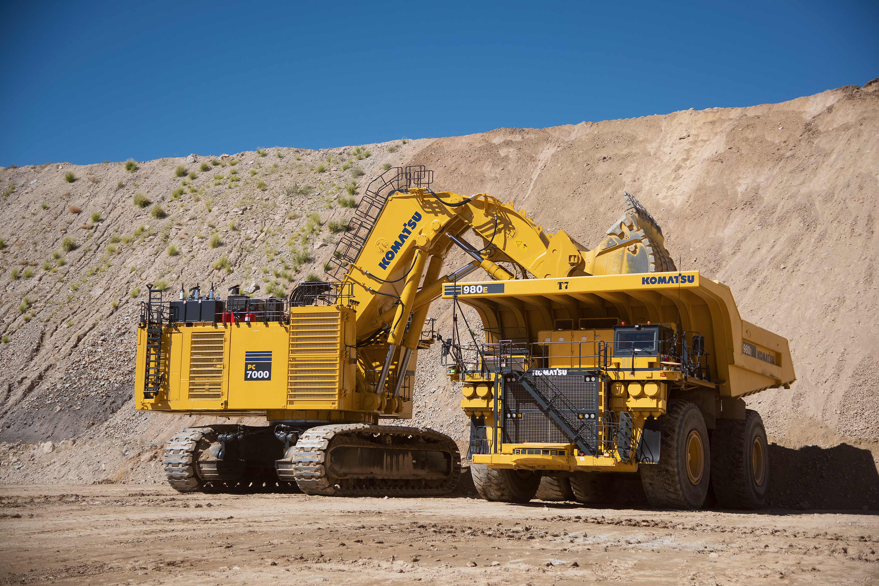 a mining excavator and dump truck working together in mid day sun with blue sky and brown sandy ground