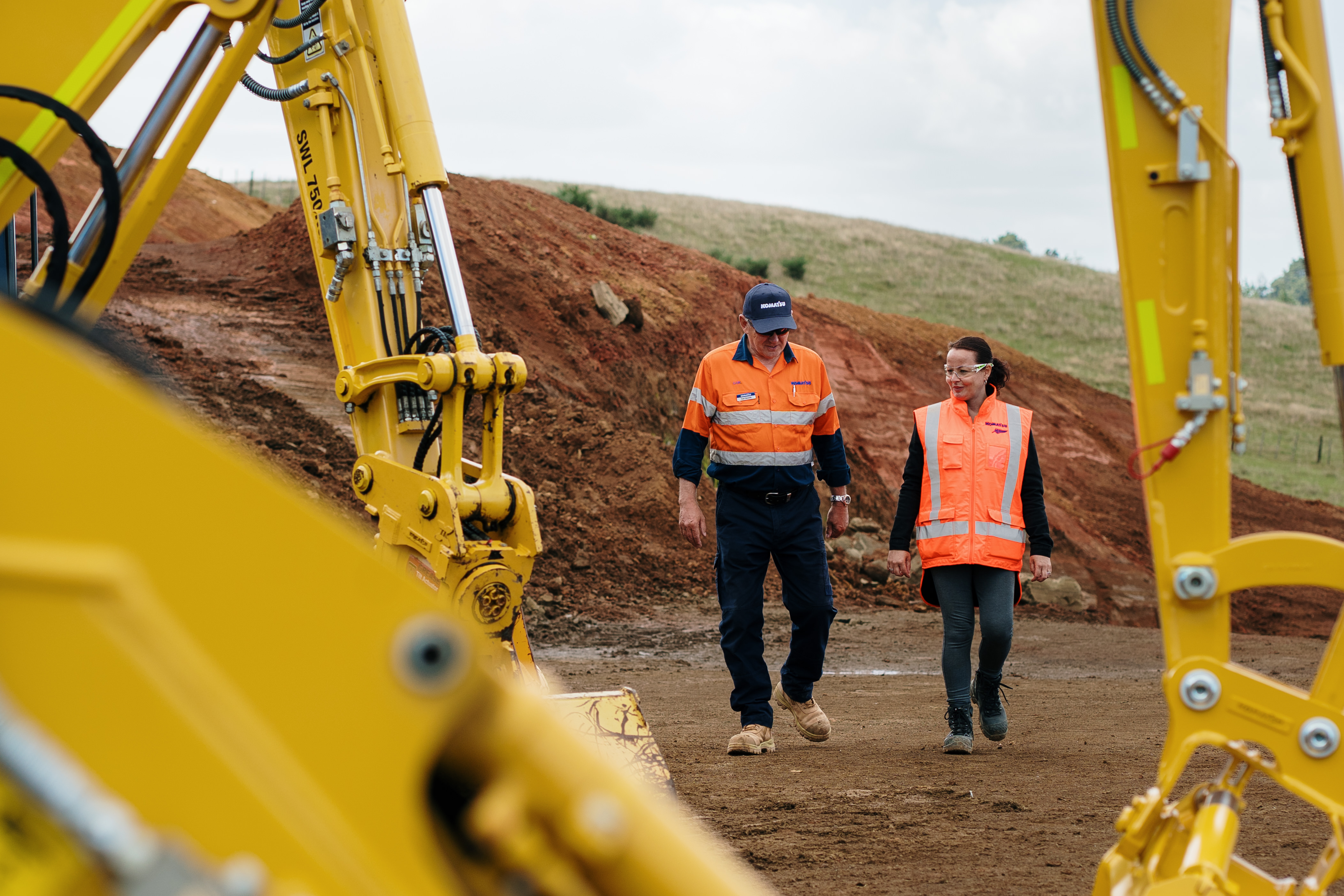 Two people walking a job site framed by a piece of equipment