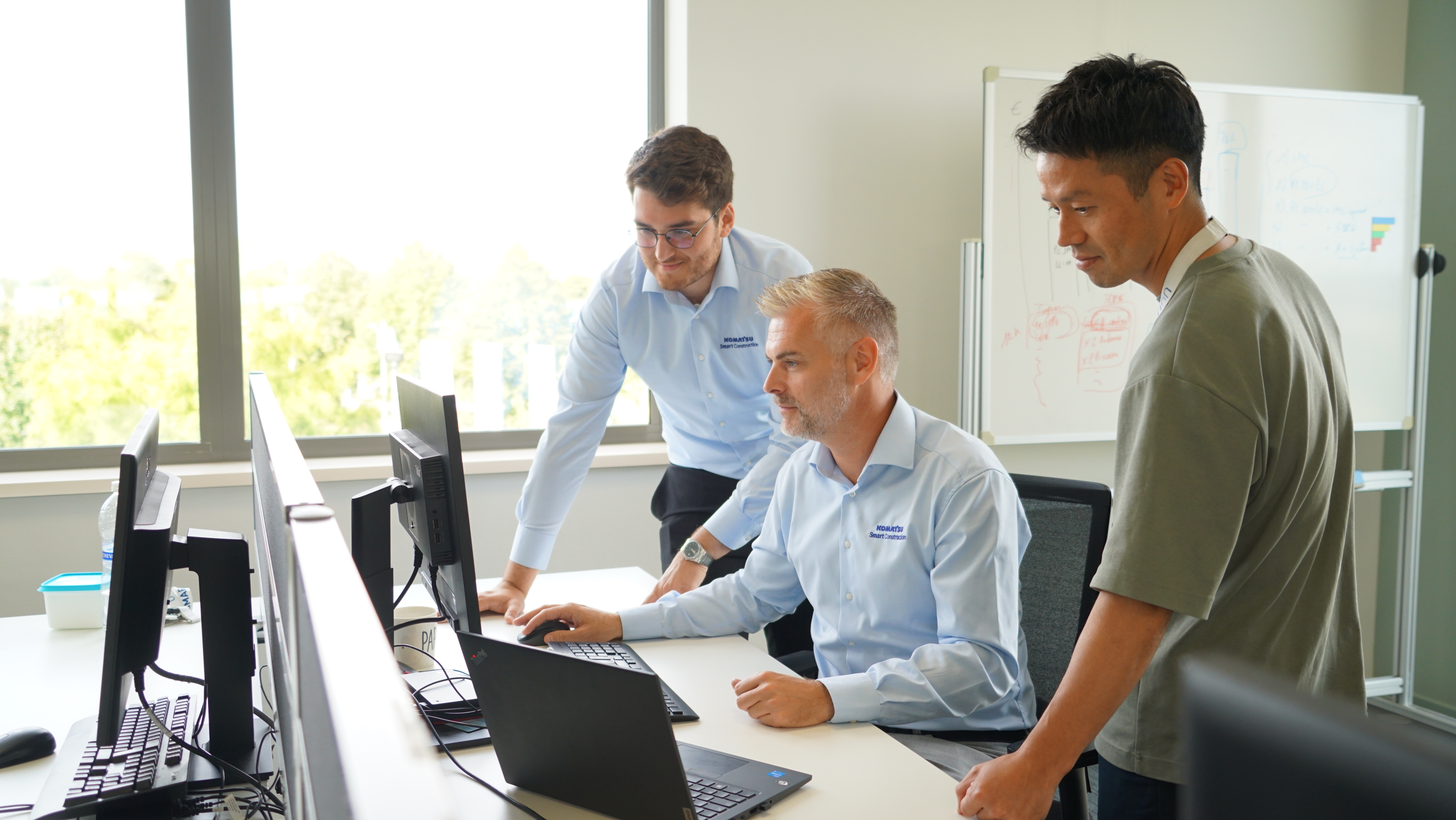 Bart Vingerhoets, Senior Commercial Manager for Komatsu Europe, in office sitting at the computer with two other colleagues standing beside him