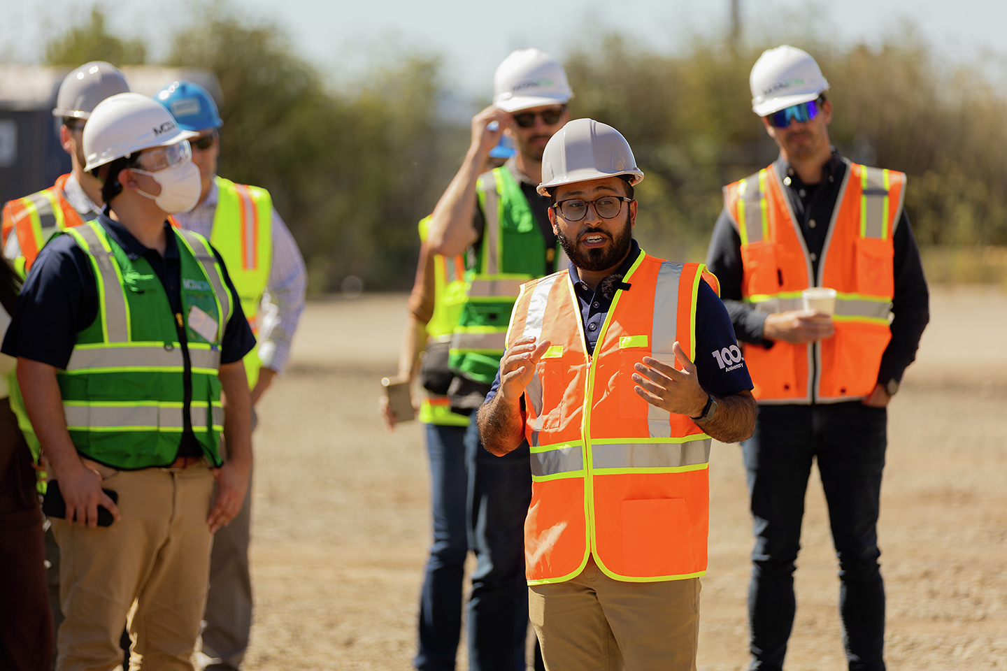 Worker leads a briefing with a group of team members at an outdoor work site.