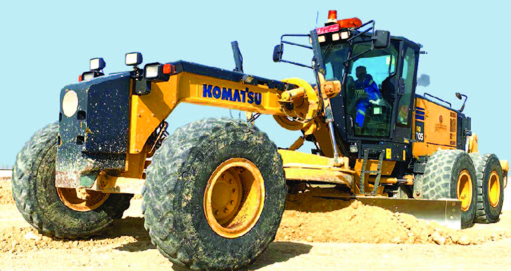 تقوم آلة تمهيد الطرق من Komatsu بتسوية التربة في موقع بناء، حيث يمكن ملاحظة انزياح التربة تحت شفرتها في المنتصف.