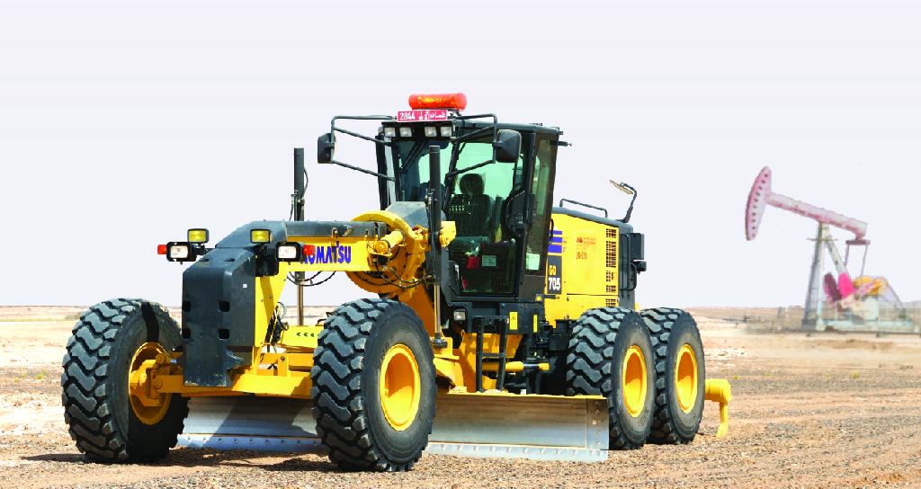 آلة تمهيد الطرق من Komatsu في منطقة شبيهة بالصحراء، مع مضخة نفط في الخلفية.