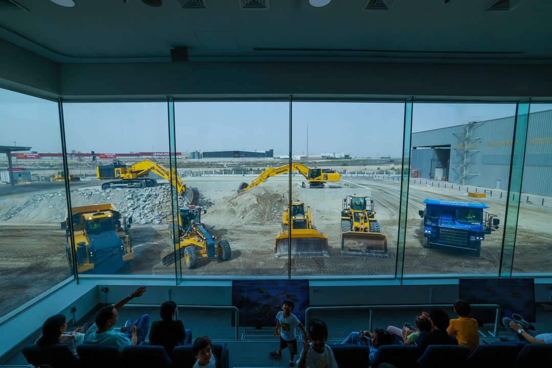 أطفال وبالغون جالسون خلف الزجاج، يراقبون مركبات البناء العاملة