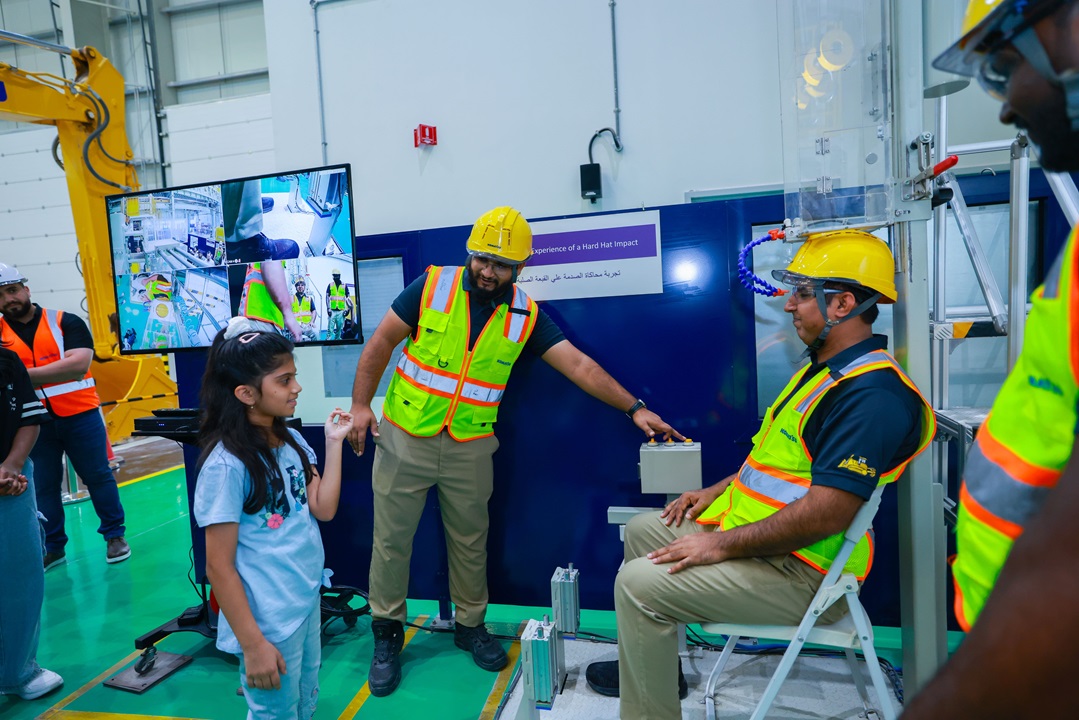 رجل جالس في منصة اختبار ميكانيكية بينما يشير آخر إلى أزرار التحكم؛ وأطفال وبالغون يشاهدون عرضًا توضيحيًا حول السلامة