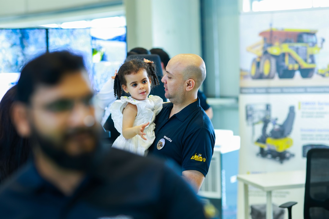 رجل يرتدي قميصًا كحلي اللون يحمل طفلة ترتدي فستانًا أبيض في حفل داخلي