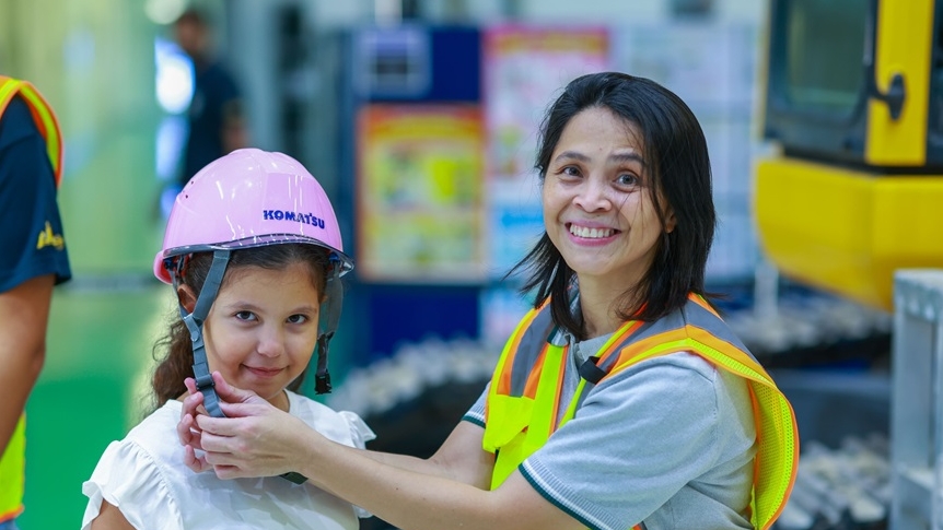 امرأة تضبط خوذة أمان وردية من ماركة Komatsu على رأس فتاة مبتسمة