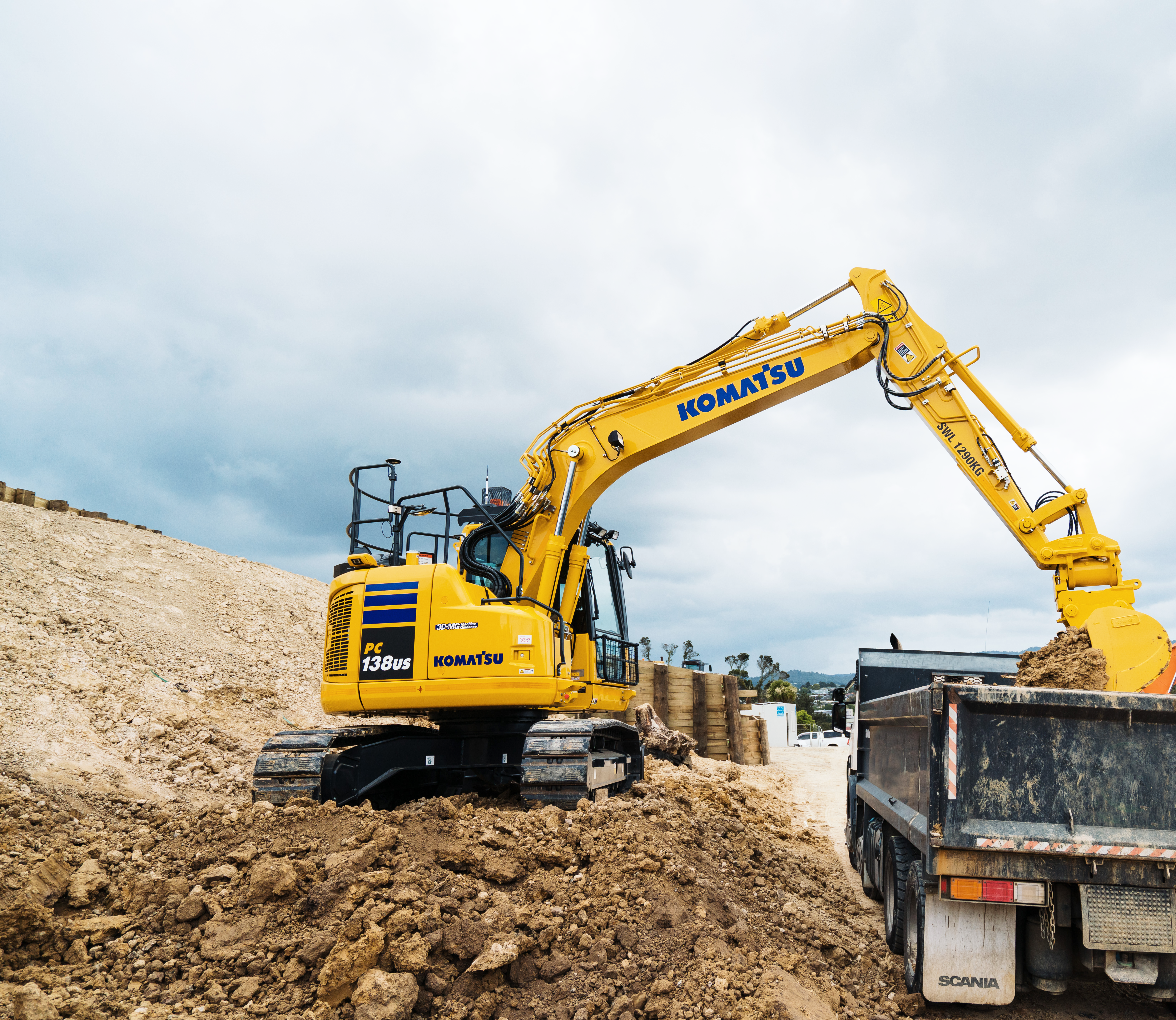 A Komatsu PC138US excavator on a construction site loading a haul truck.