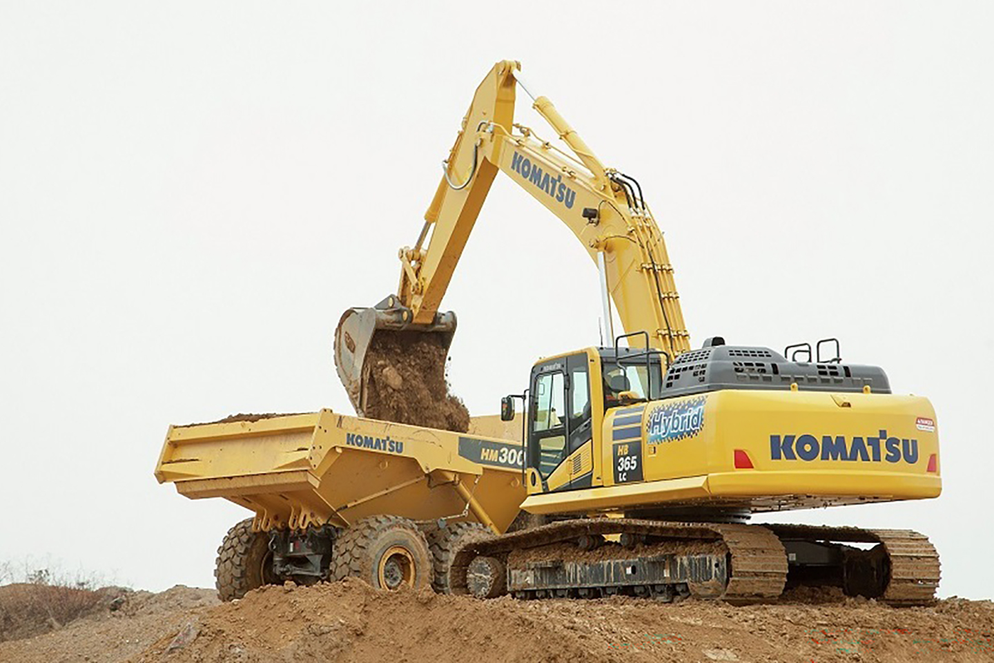 A Komatsu excavator loading a dump truck on a construction site.