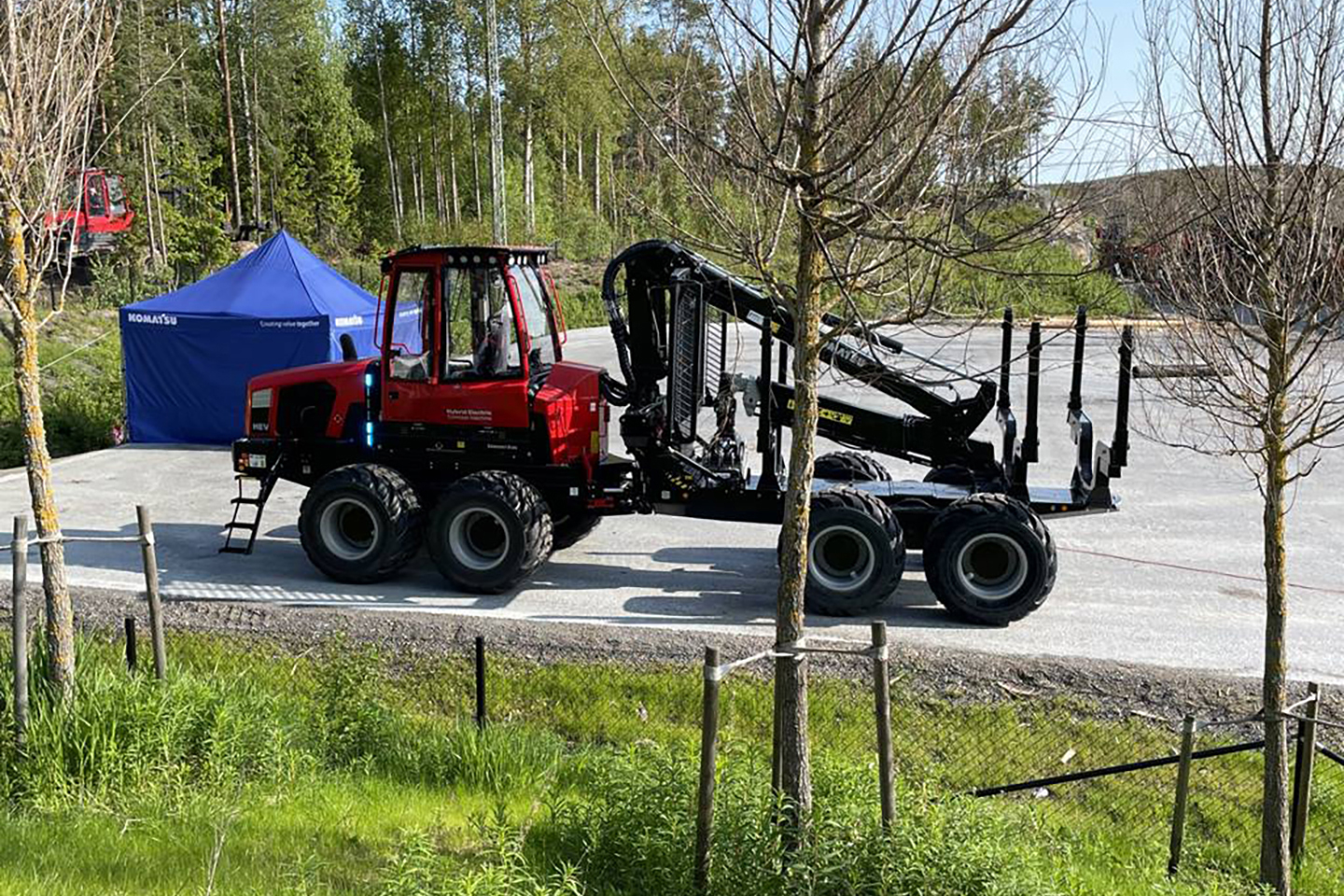 A Komatsu Forestry machine is on a concrete floor outdoors amongst trees.