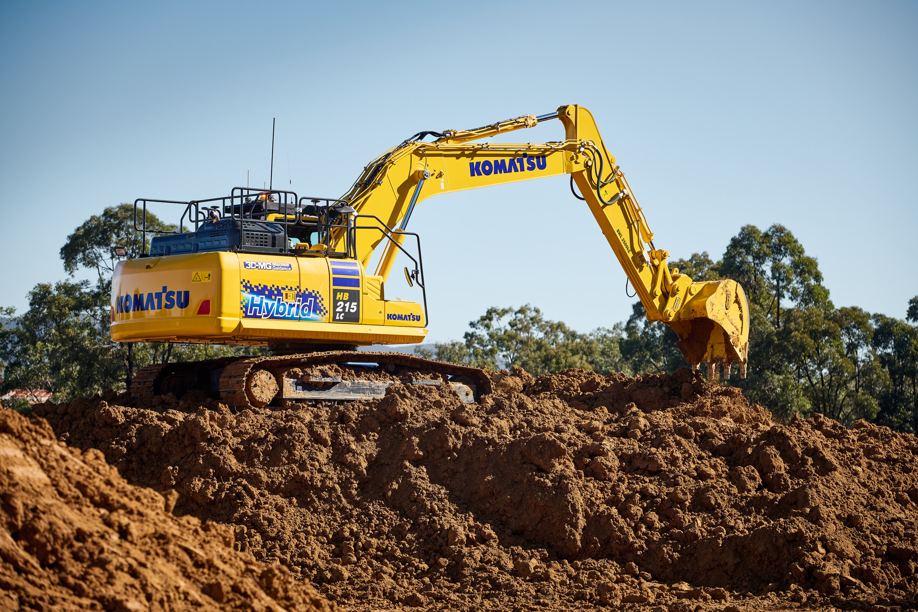 A Komatsu hybrid excavator on a mound of dirt, tipping dirt out of its bucket in a construction site.