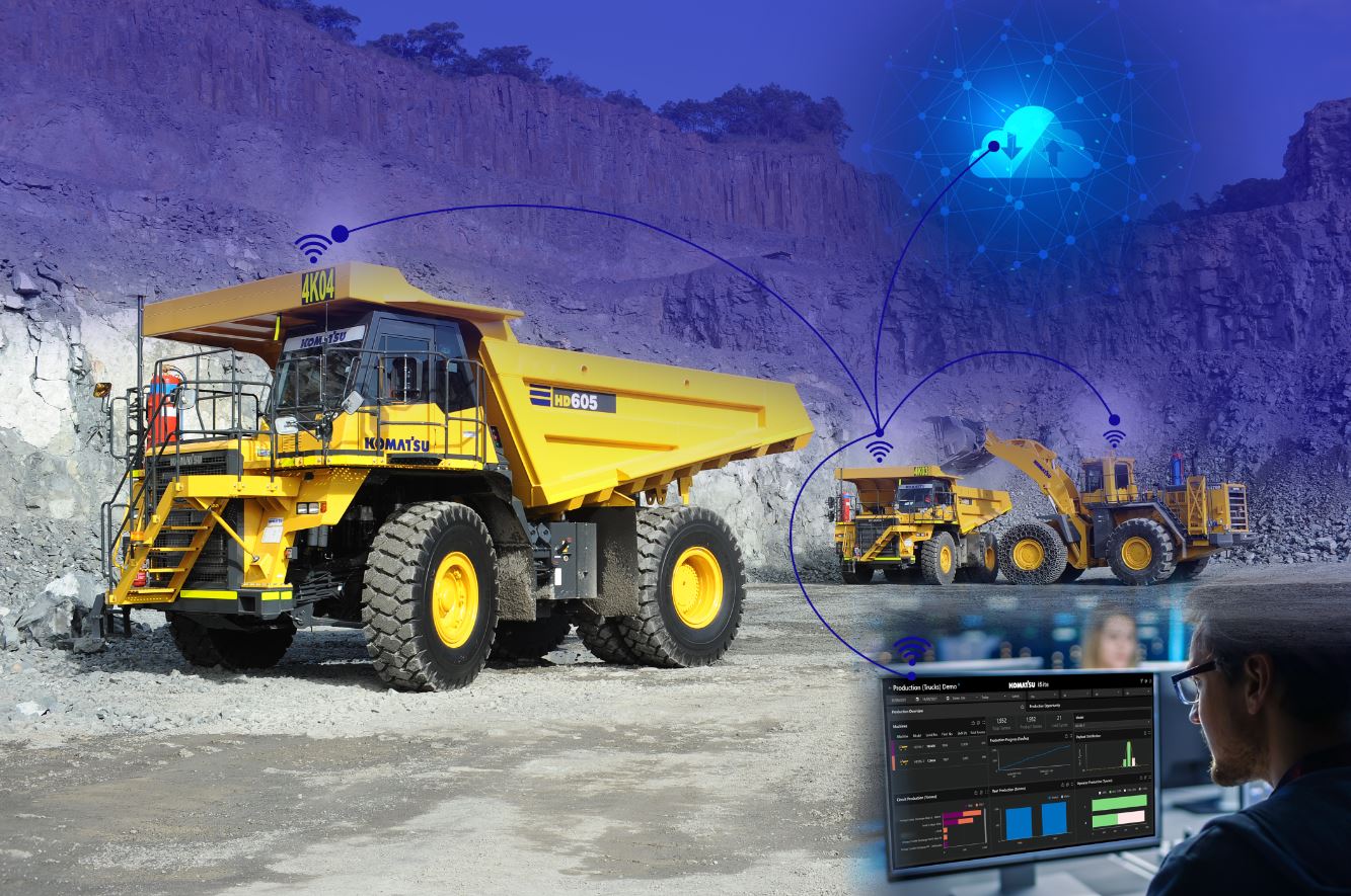 A large yellow truck is operating in a quarry, surrounded by rocky terrain. Digital graphics overlay the scene, depicting wireless connectivity and cloud symbols. In the foreground, a person is monitoring data on a computer screen, suggesting remote operations or automation.