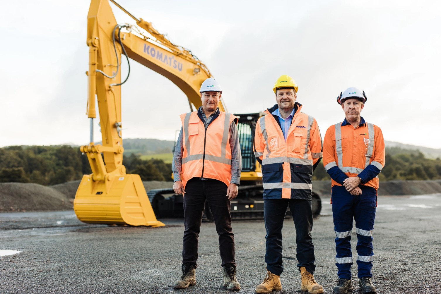 Three workers stand in front of equipment