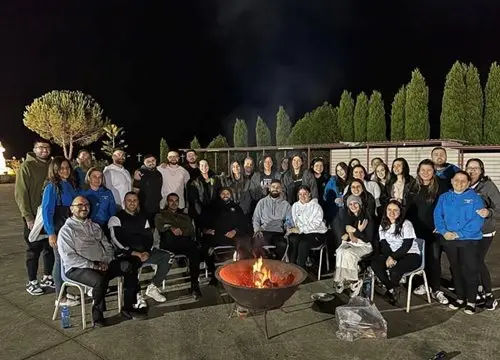 Large group of people sitting and standing around an outdoor fire pit at night
