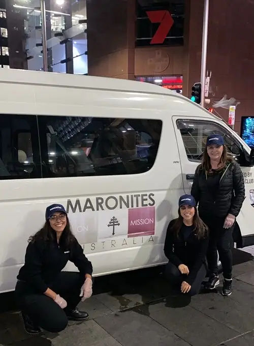 Three people posing in front of a van of marionites mission