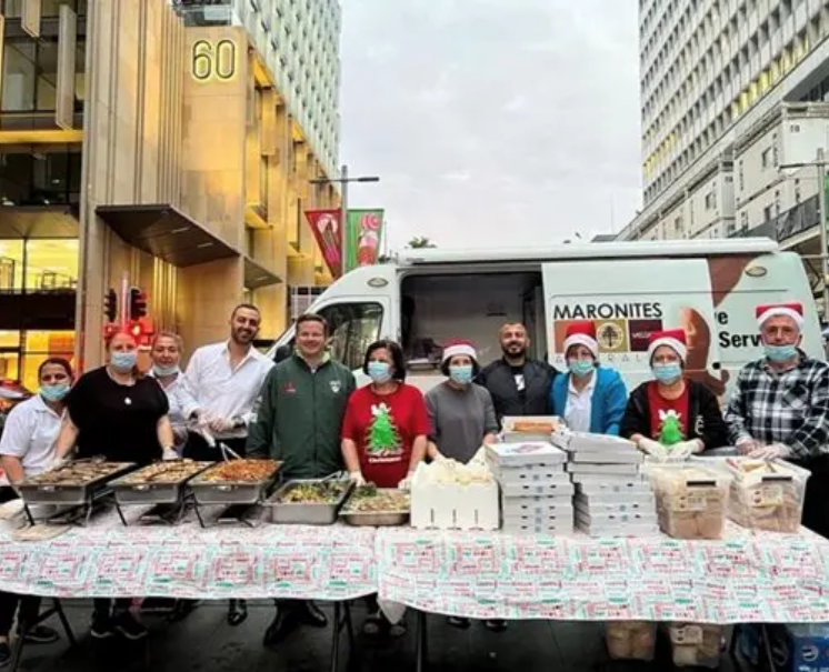 Group of people standing behind a long table filled with trays of food