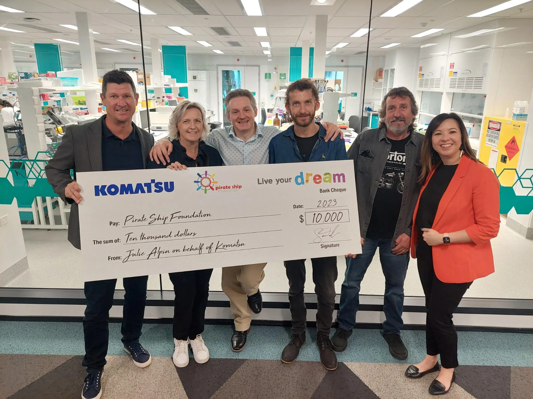Group of people standing together with large Komatsu Live Your Dream cheque prop