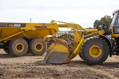 A Komatsu HM300 dump truck and wheel loader shown on a construction site.