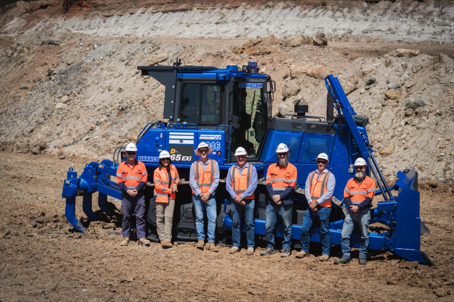 Group of workers in safety gear standing in front of a large blue Komatsu bulldozer at a construction site.