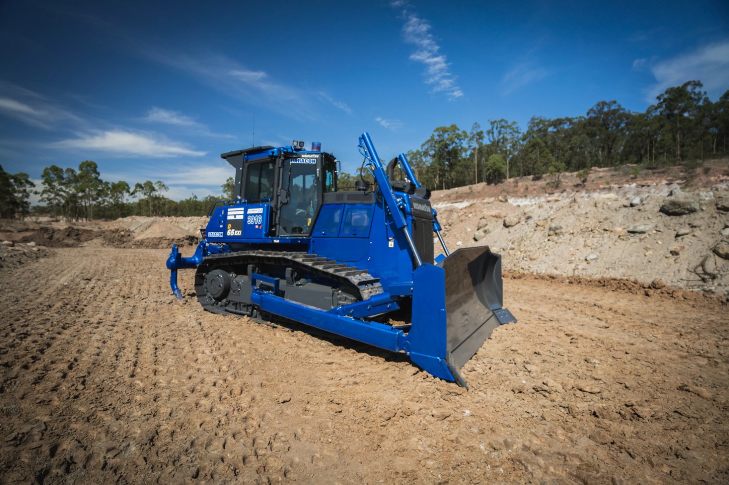 A Komatsu D165-EXi bulldozer on a bare dirt terrain under a clear sky.