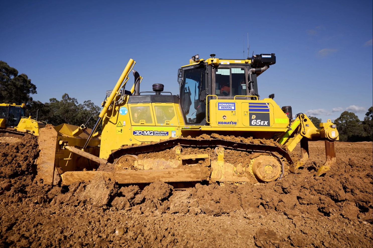 A large yellow Komatsu dump truck driving on a gravel road with snow-dusted rocky terrain in the background.