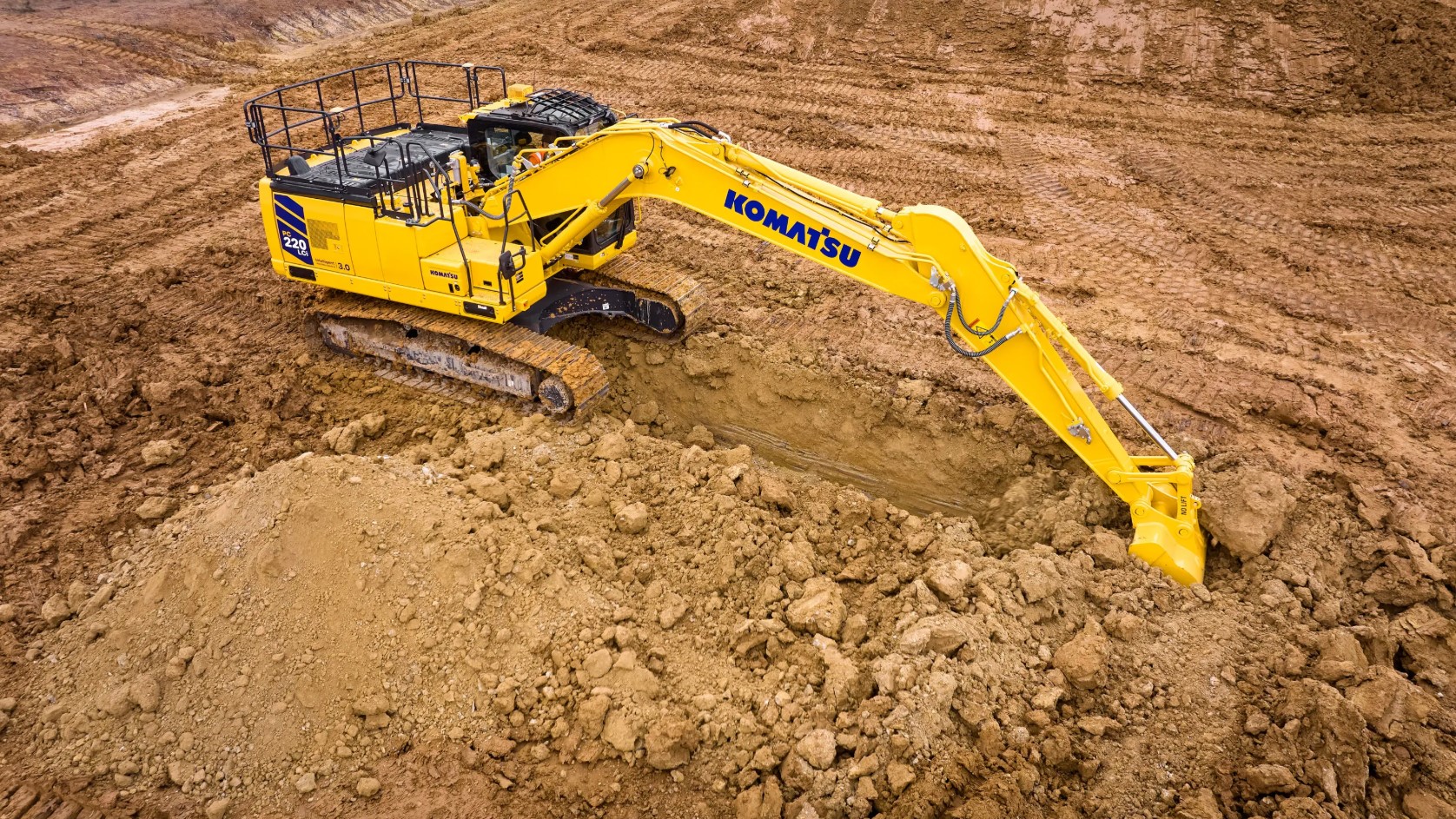 A Komatsu excavator digging into the ground on a worksite.