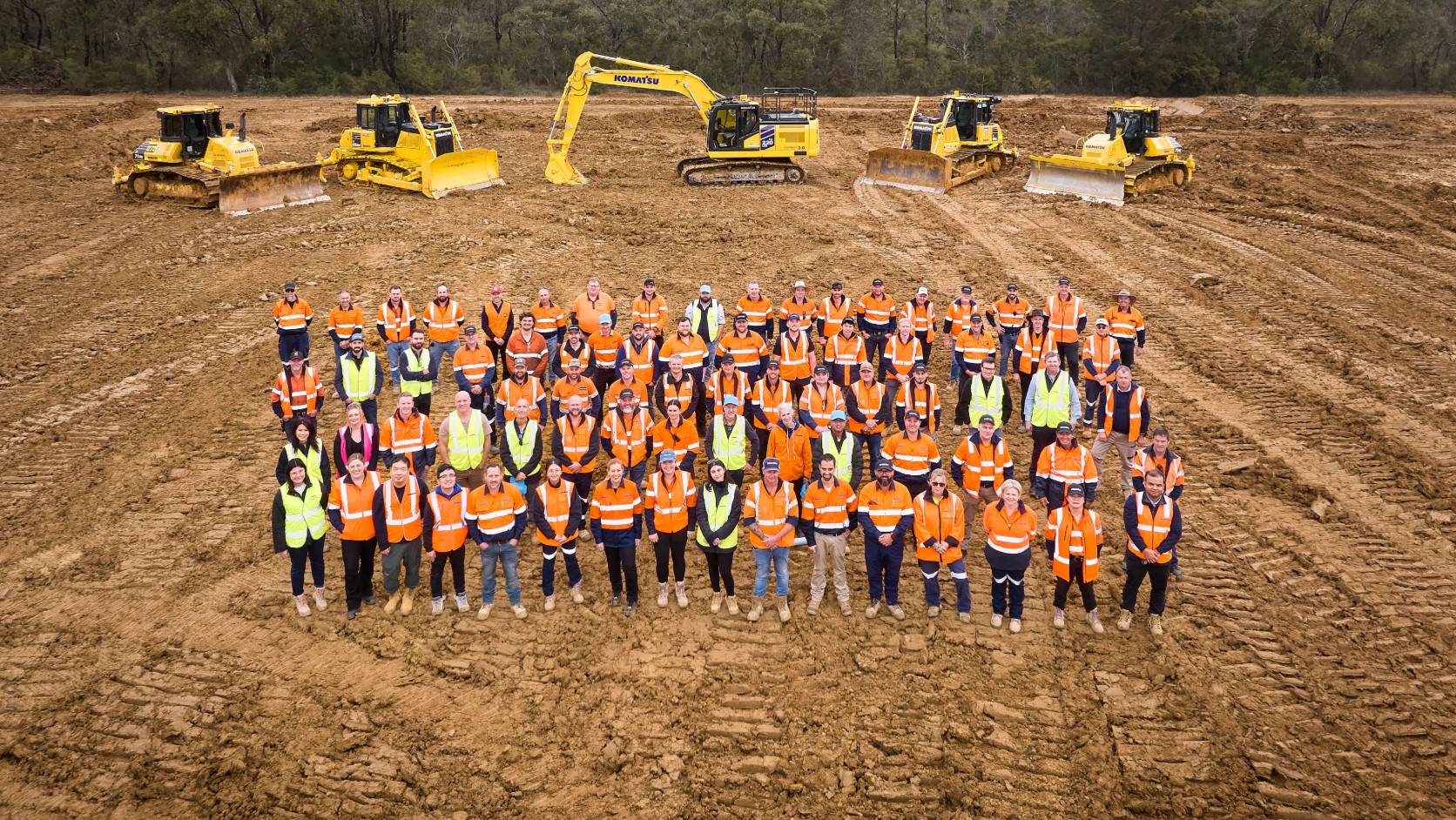 Group of people in high-visibility vests standing together in front of heavy machinery on a construction site.