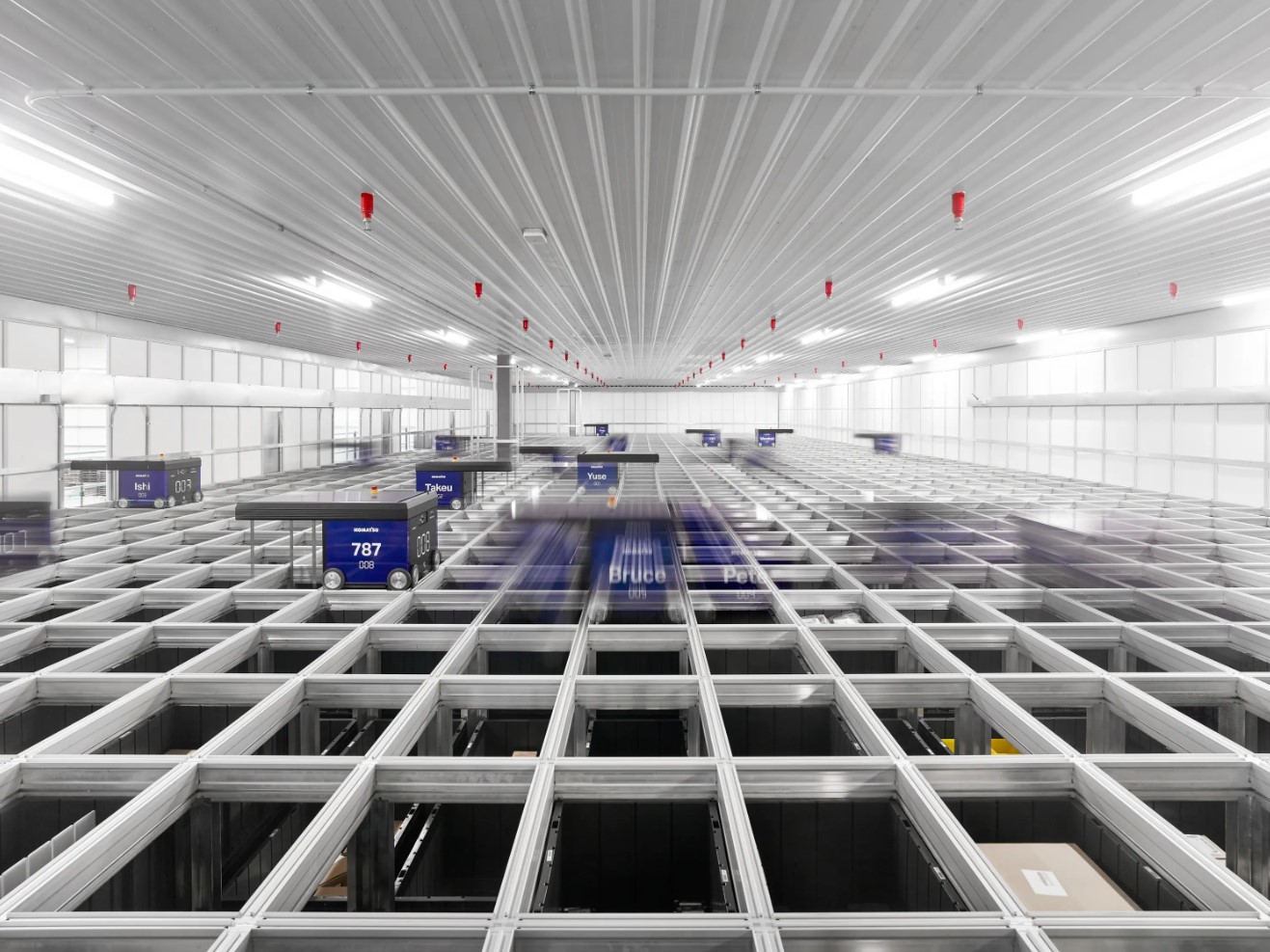  Interior of a fulfillment center with packages and conveyor systems visible under a vast, brightly lit ceiling.
