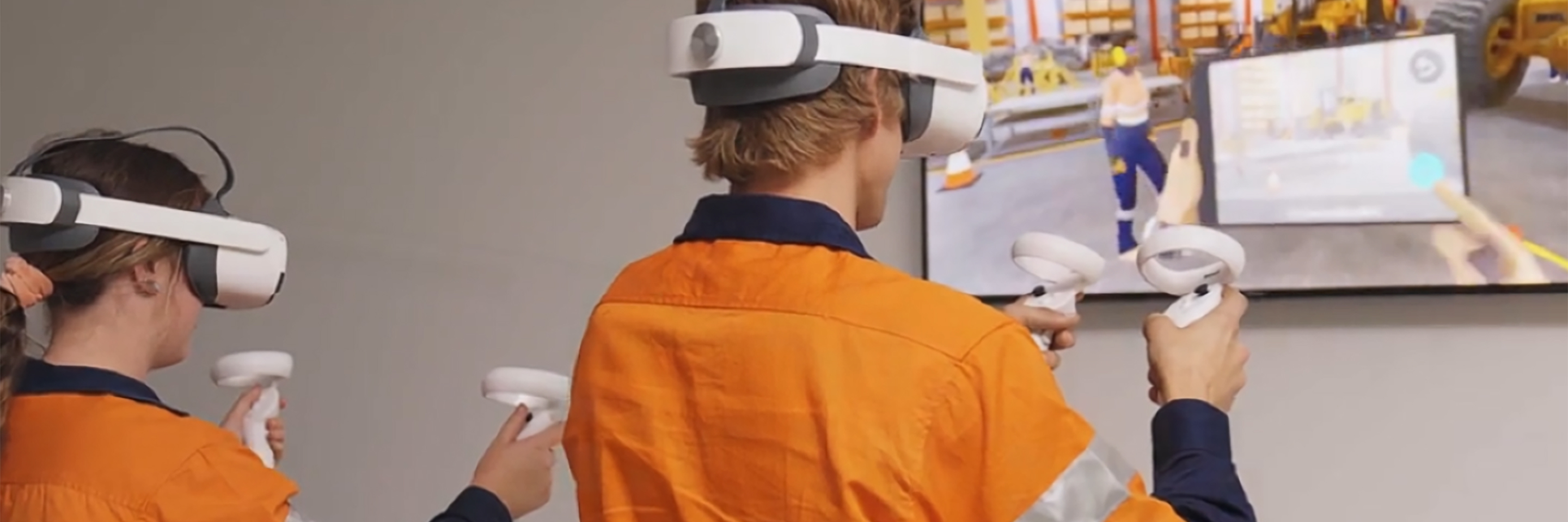 Two individuals in orange high visibility clothing, each wear a virtual reality headset for training purposes.
