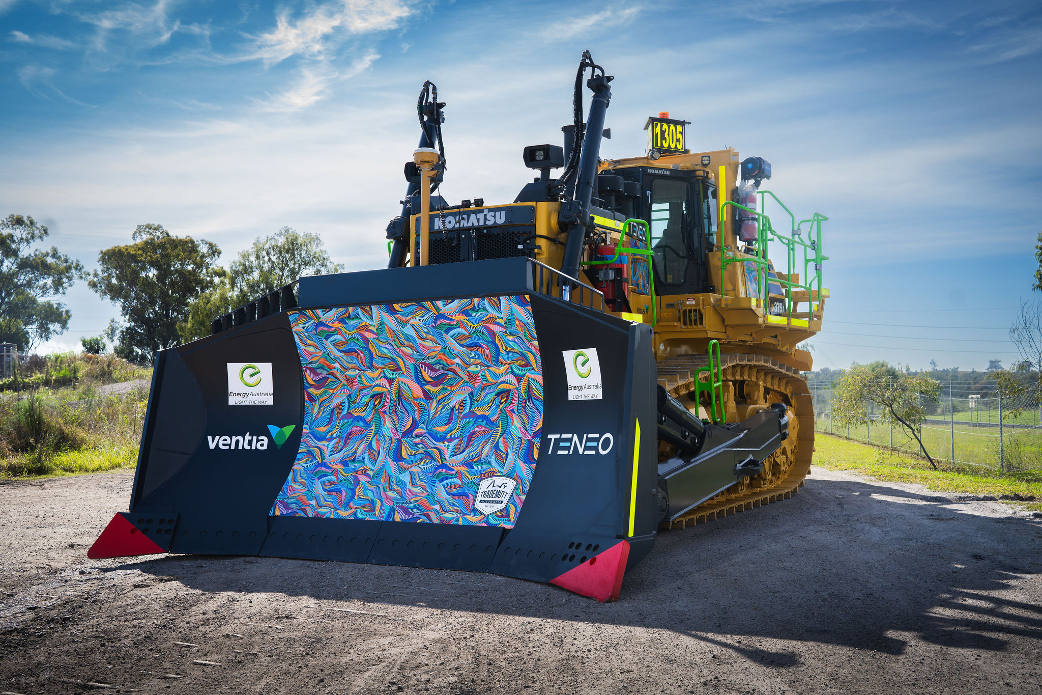 A Komatsu bulldozer with a colorful decal on the blade, parked outdoors on a sunny day.