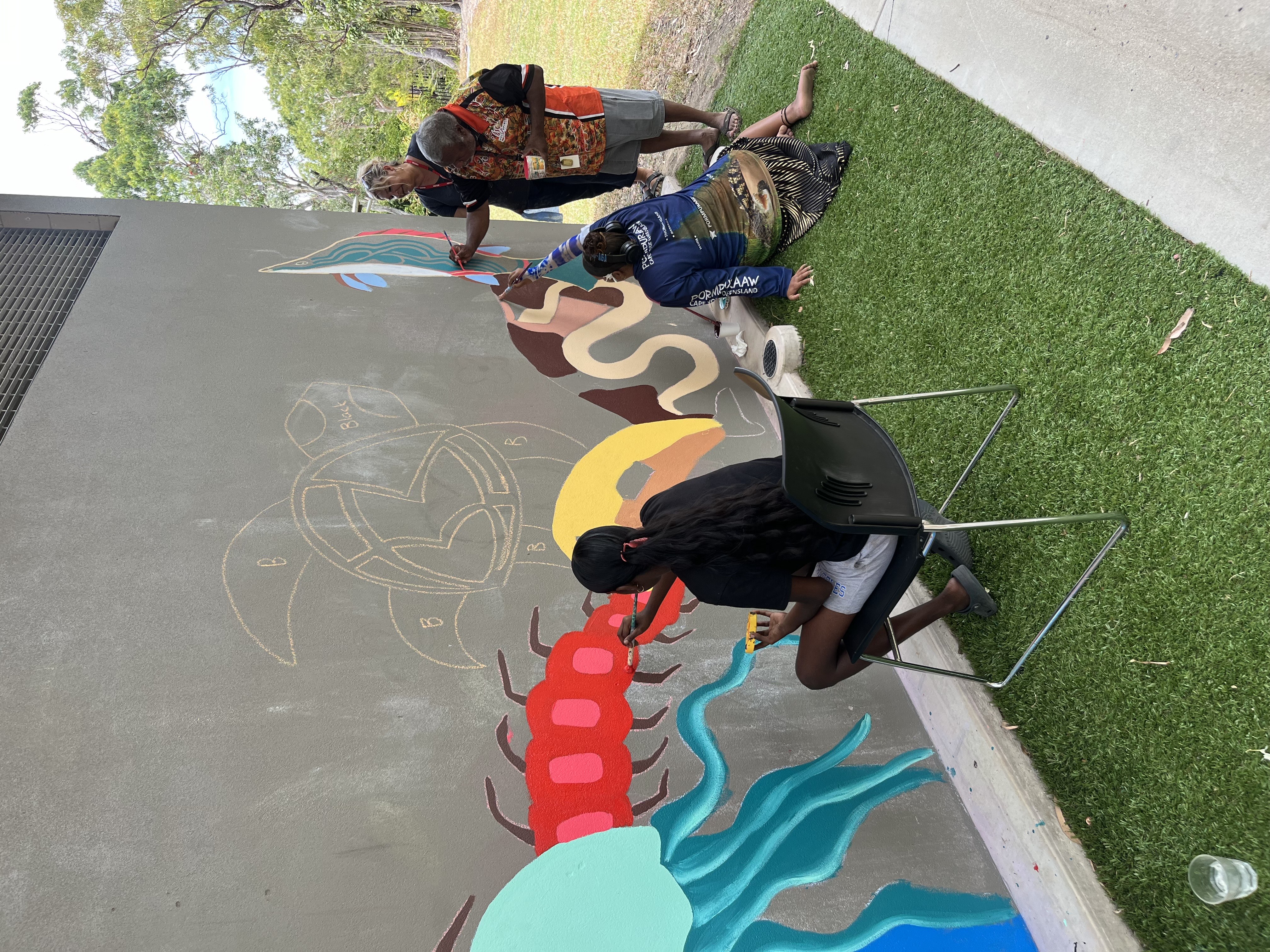 Three people are painting a colorful mural on a sidewalk.