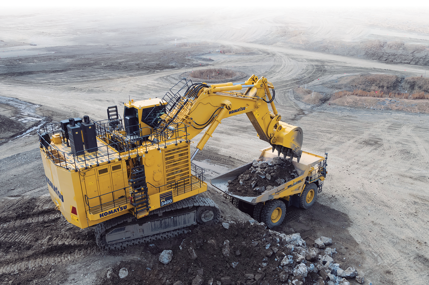 A Komatsu excavator loading dirt into the bed of a large mining dump truck in a mine.