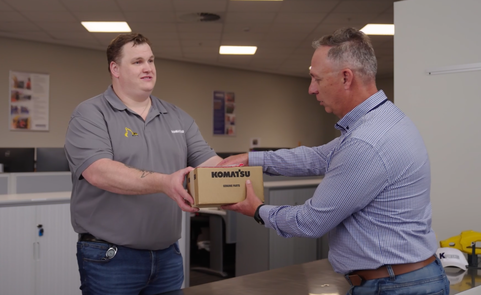 Komatsu worker handing box of Komatsu genuine parts to customer.