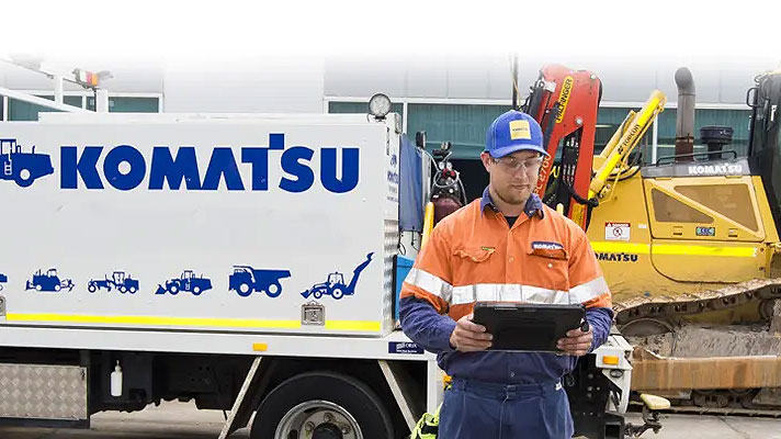 Man holding a notebook in front of a labelled Komatsu truck and a Dozer D65X 
